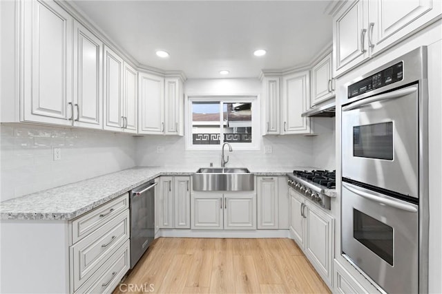 kitchen with appliances with stainless steel finishes, white cabinetry, a sink, and light wood finished floors