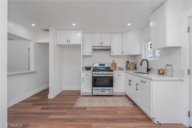 kitchen with light countertops, stainless steel gas range oven, white cabinetry, and under cabinet range hood