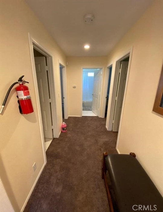 hall with baseboards and dark carpet