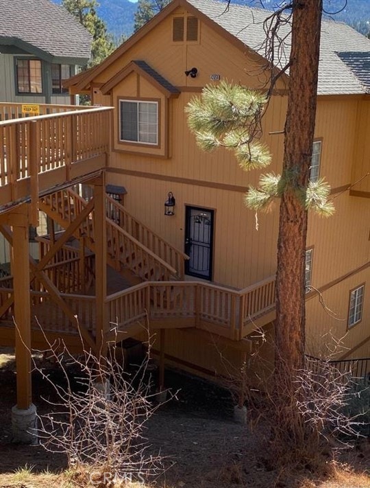 rear view of house featuring a shingled roof, stairway, and a wooden deck