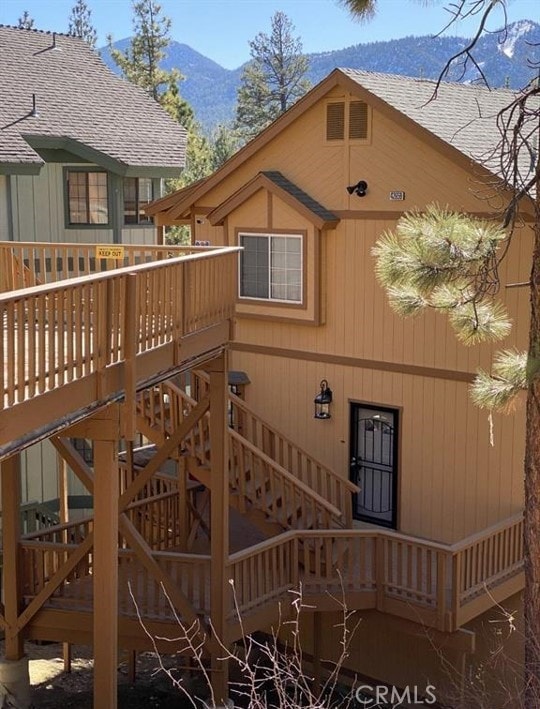 view of side of home with a deck with mountain view, a shingled roof, and stairway