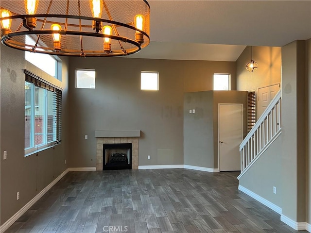 unfurnished living room with a high ceiling, a tiled fireplace, dark wood finished floors, and baseboards