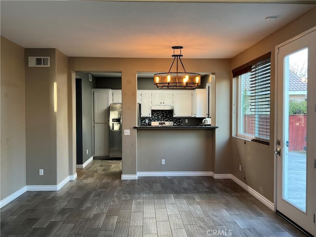 kitchen with dark countertops, stainless steel fridge, decorative light fixtures, and white cabinetry