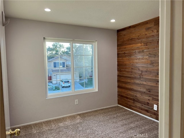 carpeted empty room with baseboards, recessed lighting, and wooden walls