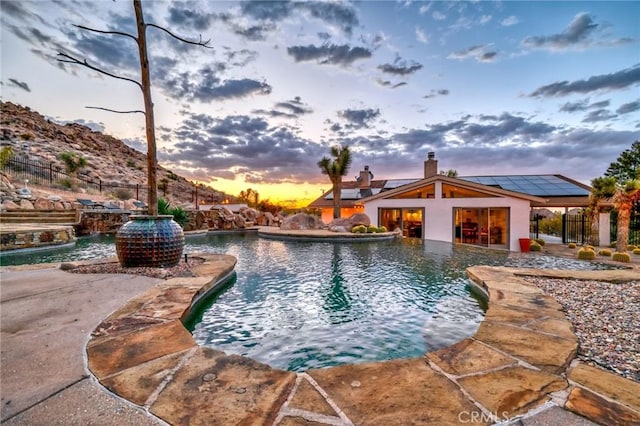 pool at dusk with a patio area, fence, and an outdoor pool