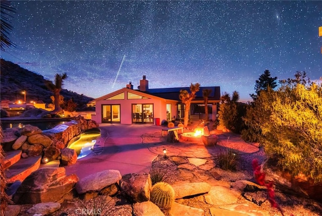 back of property with a chimney, a patio area, an outdoor pool, and a fire pit