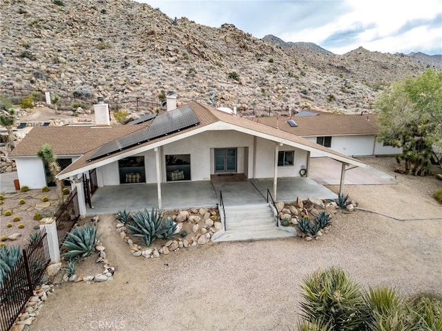 view of front of property with stucco siding, solar panels, a patio area, a mountain view, and a fenced backyard