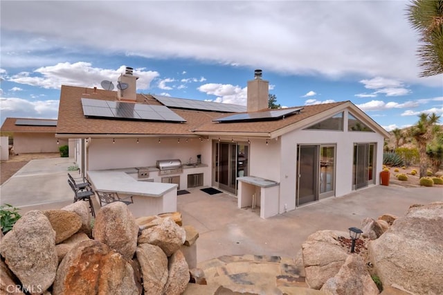 back of house featuring stucco siding, solar panels, a patio, and area for grilling