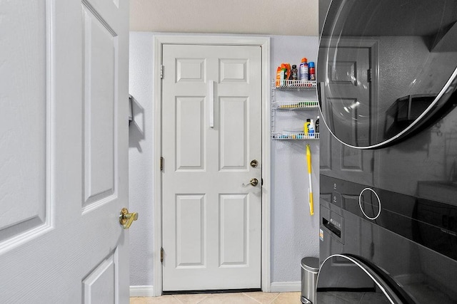 clothes washing area with stacked washer / drying machine, laundry area, baseboards, and tile patterned floors