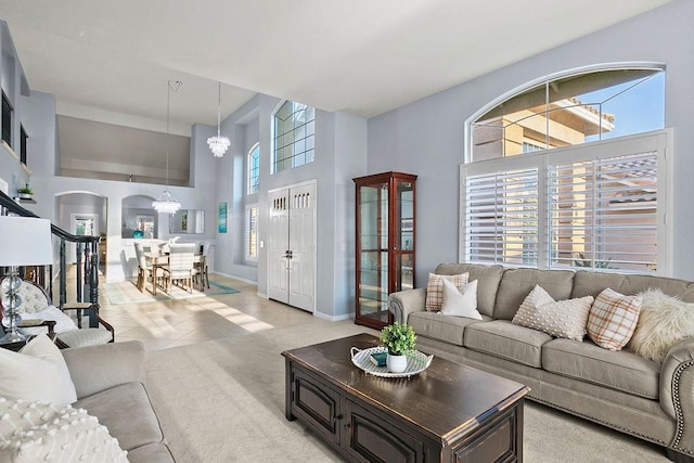 living area with arched walkways, a notable chandelier, light carpet, a towering ceiling, and baseboards