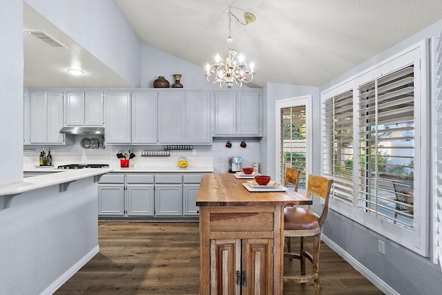 kitchen with vaulted ceiling, a notable chandelier, under cabinet range hood, baseboards, and dark wood-style flooring