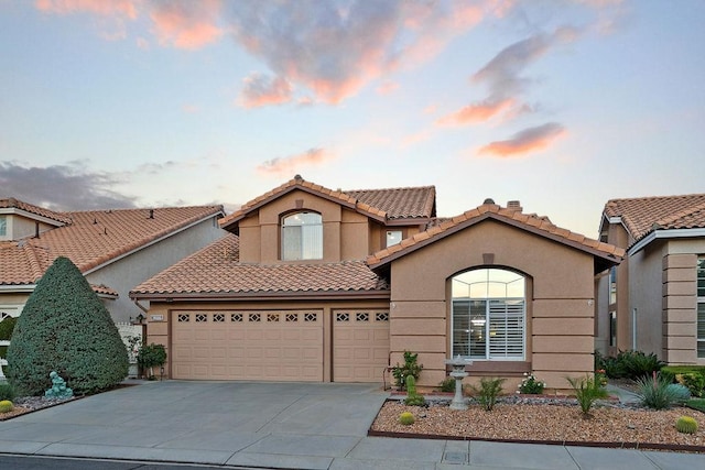 mediterranean / spanish-style home featuring a garage, a tiled roof, concrete driveway, and stucco siding