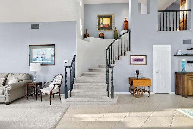 staircase featuring visible vents, a towering ceiling, baseboards, and tile patterned floors