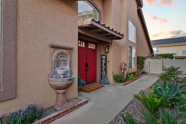 exterior entry at dusk with a gate, stucco siding, and fence