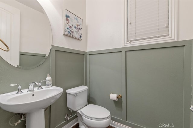 bathroom with wainscoting, a sink, toilet, and a decorative wall