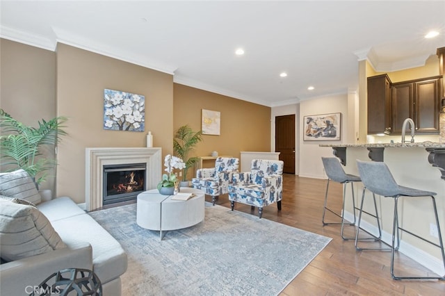 living room with light wood-type flooring, crown molding, a lit fireplace, and recessed lighting