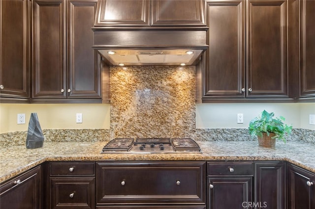 kitchen featuring dark brown cabinetry, custom range hood, stainless steel gas cooktop, and light stone counters