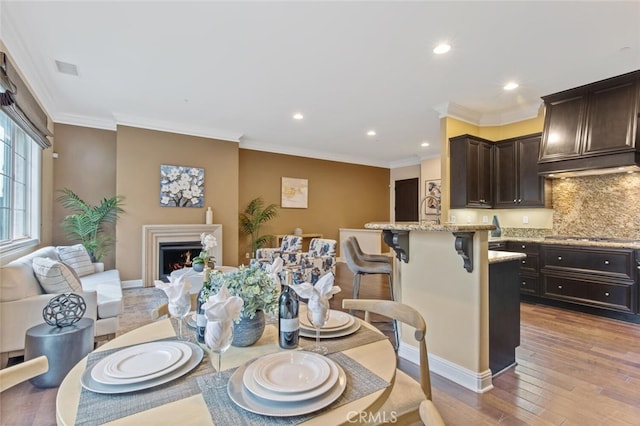 dining room featuring light wood finished floors, a warm lit fireplace, crown molding, and recessed lighting