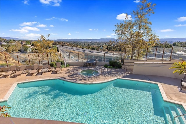 community pool with a patio area, a mountain view, a hot tub, and fence