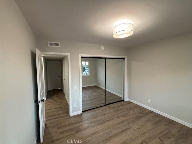 unfurnished bedroom with wood finished floors, visible vents, a closet, and baseboards