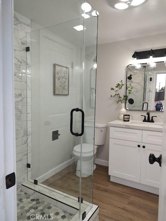 full bath featuring a shower stall, baseboards, toilet, wood finished floors, and vanity