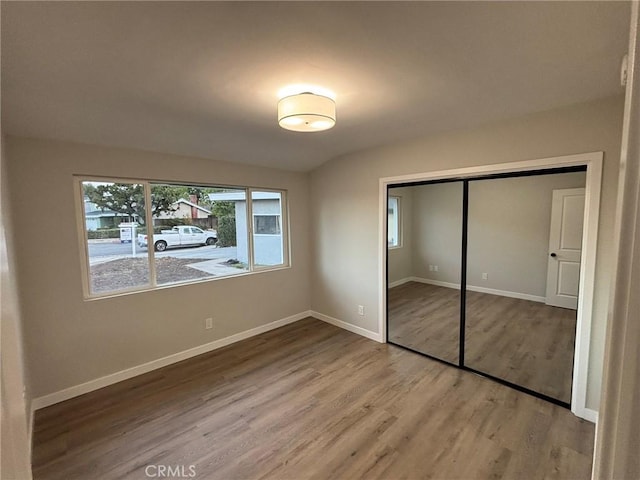 unfurnished bedroom with a closet, baseboards, wood finished floors, and vaulted ceiling