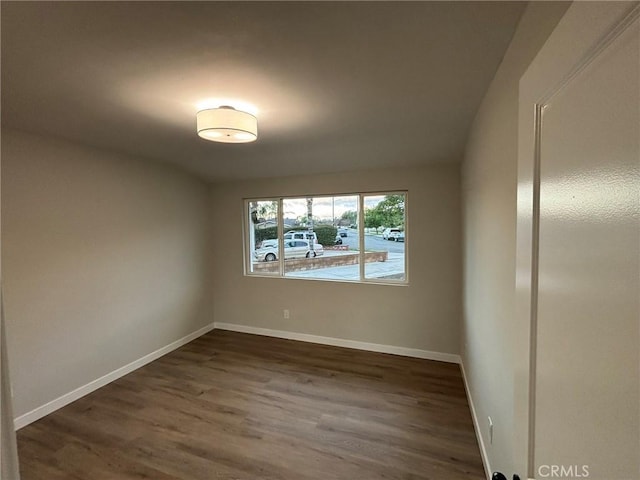 spare room featuring dark wood-type flooring and baseboards