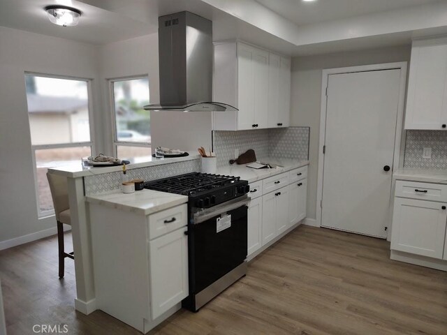 kitchen featuring gas stove, light wood-style floors, white cabinets, and wall chimney range hood