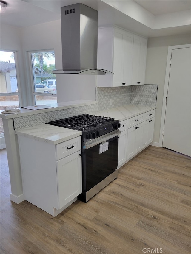 kitchen featuring stainless steel range with gas cooktop, light wood-style flooring, white cabinetry, wall chimney range hood, and tasteful backsplash