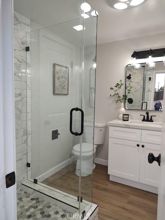 full bath with a shower stall, baseboards, toilet, wood finished floors, and vanity