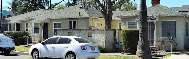 view of front facade with roof with shingles, a chimney, and stucco siding