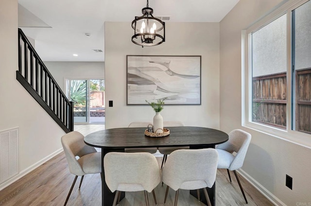 dining space with light wood finished floors, visible vents, stairway, an inviting chandelier, and baseboards