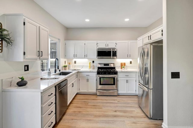 kitchen with appliances with stainless steel finishes, light stone counters, light wood-type flooring, white cabinetry, and a sink