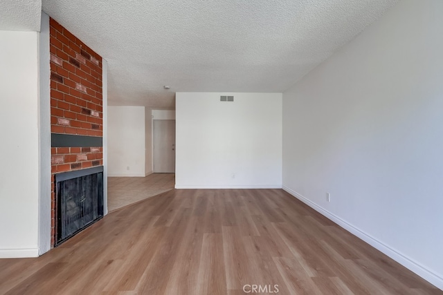 unfurnished living room featuring a textured ceiling, a fireplace, wood finished floors, visible vents, and baseboards