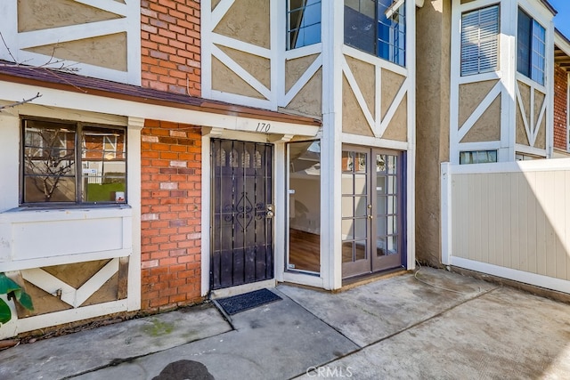 entrance to property with brick siding, fence, and stucco siding