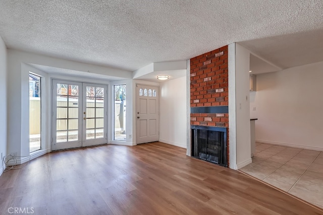 interior space with a brick fireplace, a textured ceiling, wood finished floors, and french doors