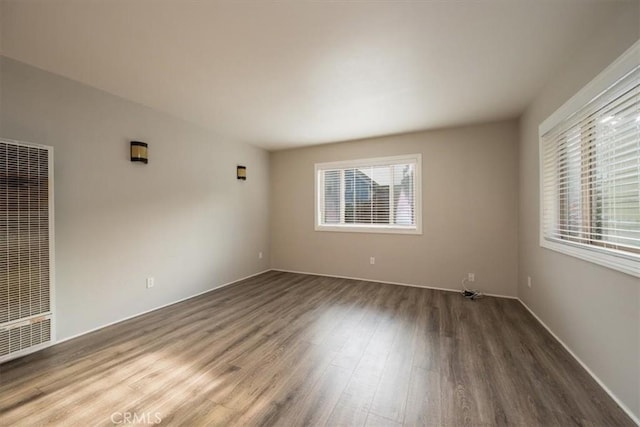 empty room featuring plenty of natural light, wood finished floors, and a heating unit