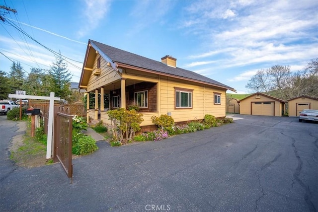 view of property exterior featuring a detached garage, fence, a chimney, an outbuilding, and driveway