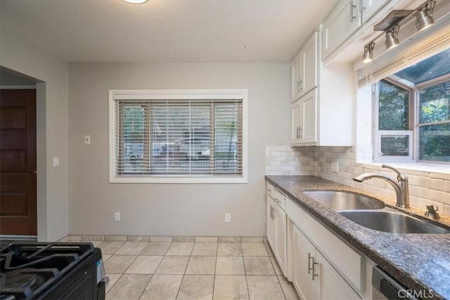 kitchen featuring dark stone countertops, a sink, white cabinets, dishwasher, and tasteful backsplash