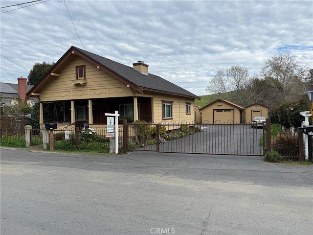 bungalow-style house with a detached garage, a fenced front yard, an outdoor structure, driveway, and a gate