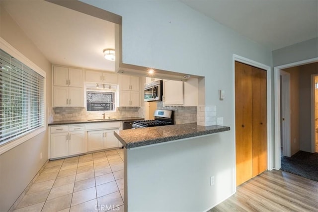 kitchen with a peninsula, a sink, appliances with stainless steel finishes, white cabinetry, and backsplash