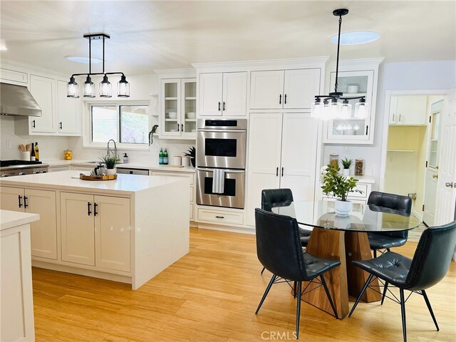 kitchen with white cabinets, stainless steel double oven, ventilation hood, light wood finished floors, and glass insert cabinets