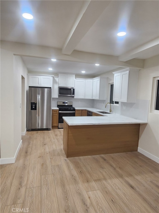 kitchen with beam ceiling, stainless steel appliances, light countertops, white cabinetry, and a sink