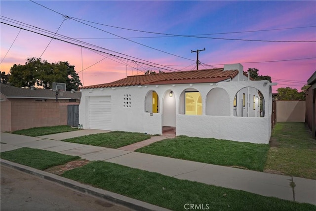 mediterranean / spanish-style home with stucco siding, concrete driveway, a front yard, fence, and a tiled roof