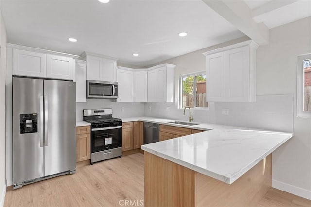 kitchen featuring a sink, stainless steel appliances, a peninsula, and light wood finished floors