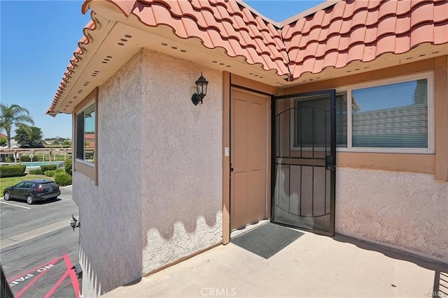 doorway to property featuring a tile roof, a patio, and stucco siding