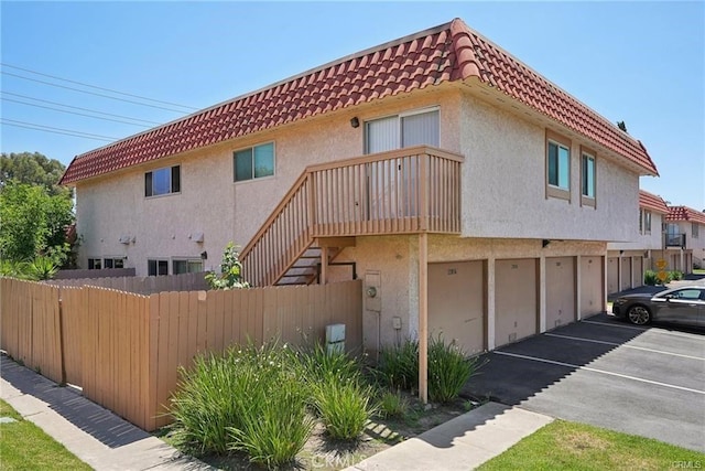 view of property exterior featuring a tiled roof, fence, and stucco siding