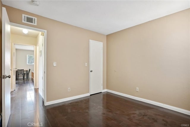 unfurnished room with visible vents, dark wood finished floors, and baseboards