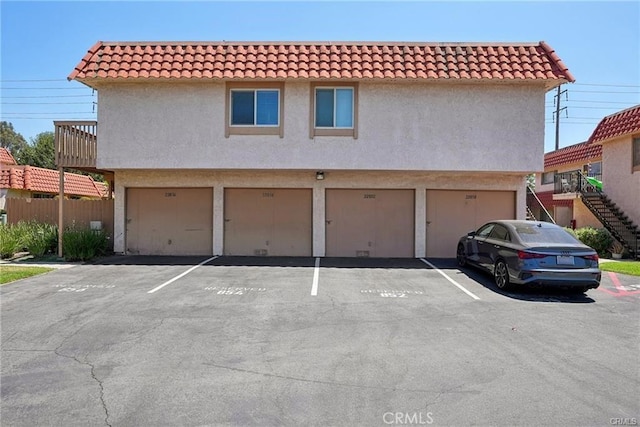 view of front of house featuring a tiled roof, uncovered parking, stairway, and stucco siding