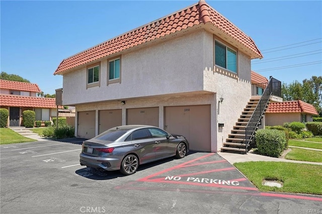 view of property featuring uncovered parking, stairway, a tile roof, and stucco siding